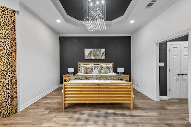 bedroom with hardwood / wood-style flooring, an inviting chandelier, crown molding, and a tray ceiling