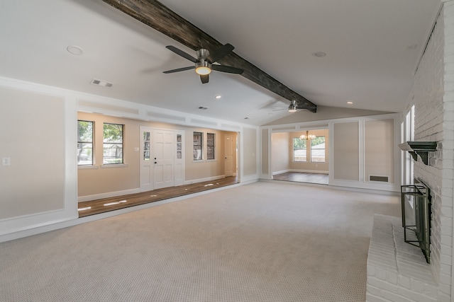 unfurnished living room with ceiling fan with notable chandelier, a fireplace, lofted ceiling with beams, and plenty of natural light