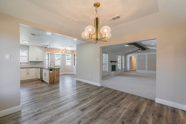 kitchen with hanging light fixtures, white cabinetry, wood-type flooring, vaulted ceiling with beams, and sink