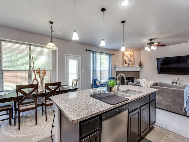 kitchen featuring hanging light fixtures, a tiled fireplace, stainless steel dishwasher, a kitchen island with sink, and sink