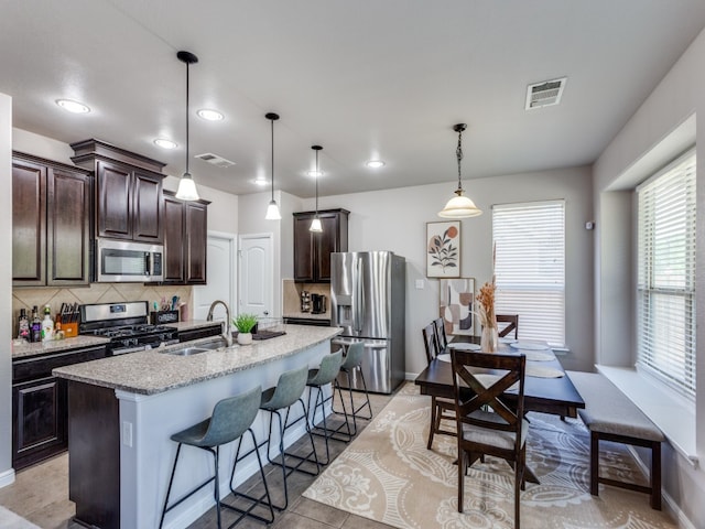 kitchen with sink, an island with sink, decorative backsplash, appliances with stainless steel finishes, and decorative light fixtures