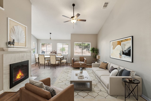 living room featuring a tile fireplace, high vaulted ceiling, light wood-type flooring, and ceiling fan