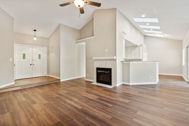 unfurnished living room featuring a high end fireplace, ceiling fan, a skylight, and dark hardwood / wood-style flooring