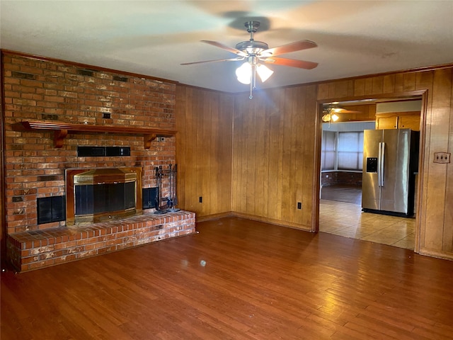 unfurnished living room featuring wood-type flooring, a fireplace, wood walls, and ceiling fan