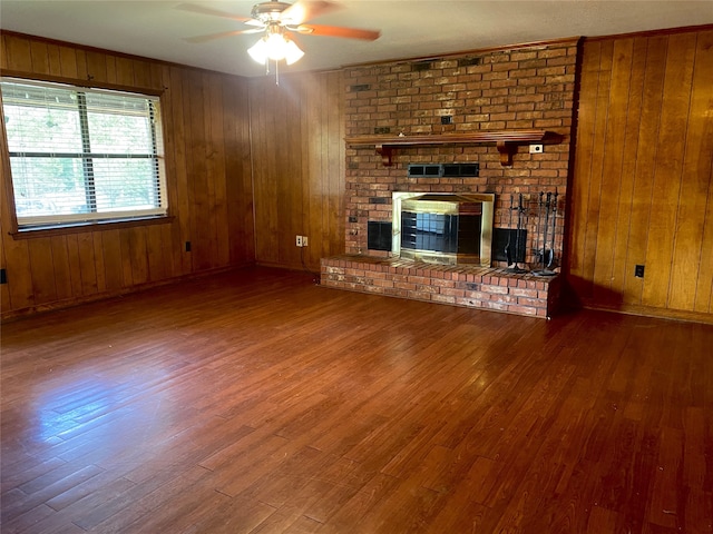 unfurnished living room with wood-type flooring, a brick fireplace, wood walls, and ceiling fan