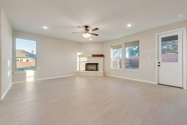 unfurnished living room with a healthy amount of sunlight, a stone fireplace, and light hardwood / wood-style flooring