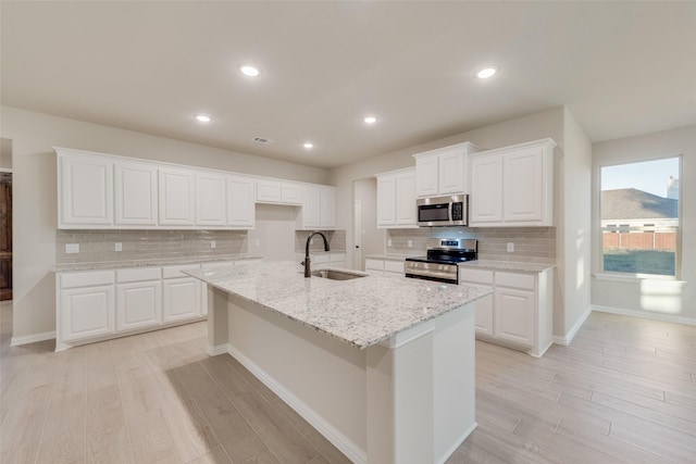 kitchen with a center island with sink, sink, light wood-type flooring, appliances with stainless steel finishes, and white cabinetry