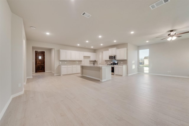 kitchen with white cabinets, an island with sink, stainless steel appliances, and light hardwood / wood-style floors