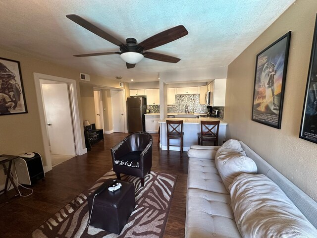 living room featuring ceiling fan, a textured ceiling, and dark hardwood / wood-style floors