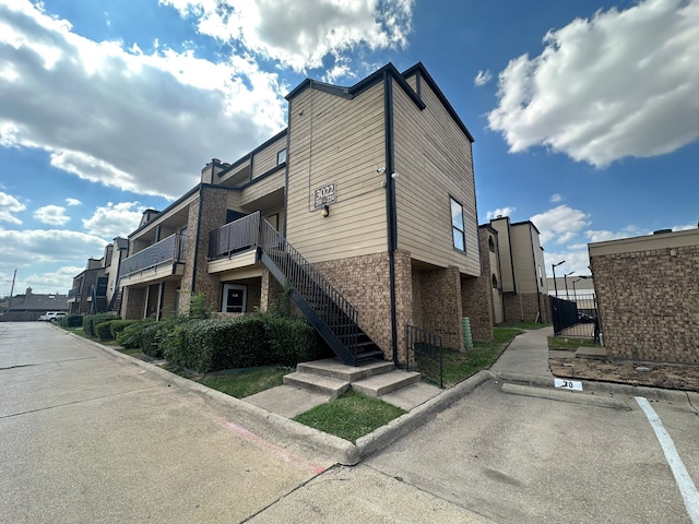 3022 Forest Ln Unit 221, Dallas, TX 75234 - view of property exterior featuring brick siding, uncovered parking, stairs, and a gate