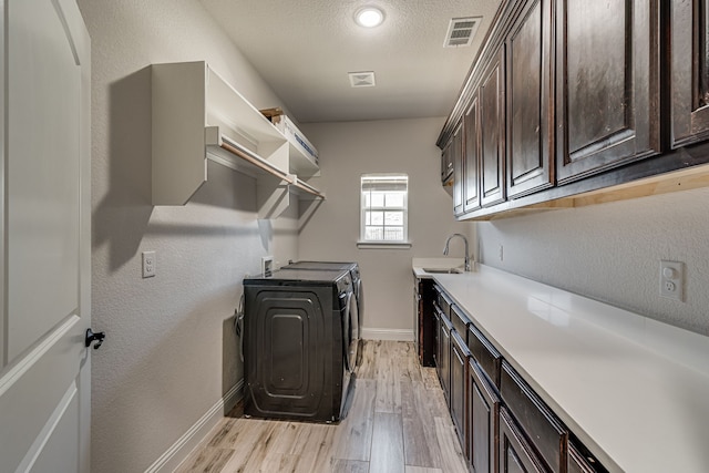 laundry room with washing machine and dryer, light hardwood / wood-style floors, a textured ceiling, cabinets, and sink