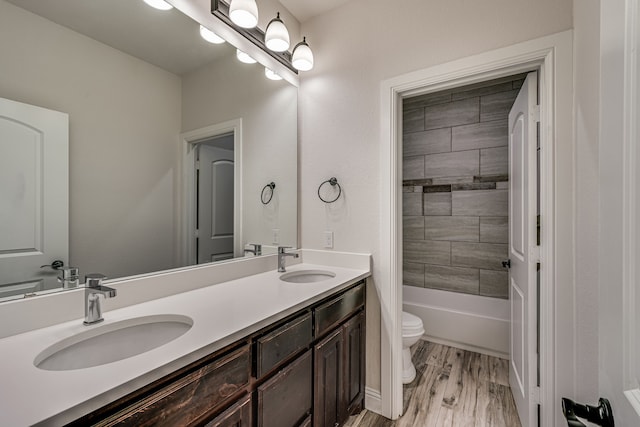 full bathroom with hardwood / wood-style floors, tiled shower / bath, vanity, and toilet