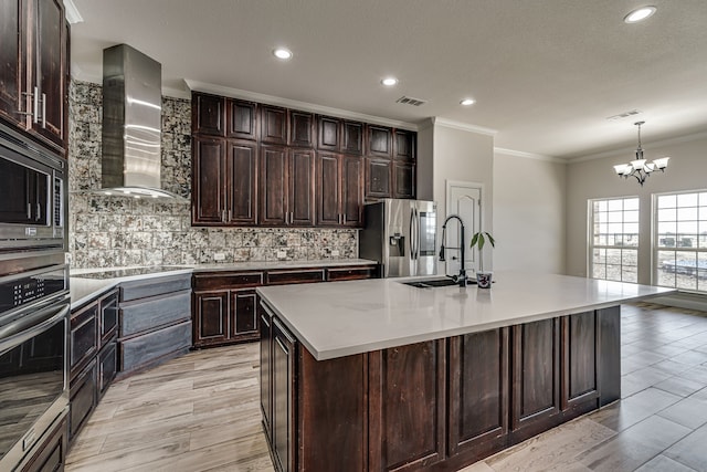 kitchen with an island with sink, sink, tasteful backsplash, wall chimney exhaust hood, and appliances with stainless steel finishes