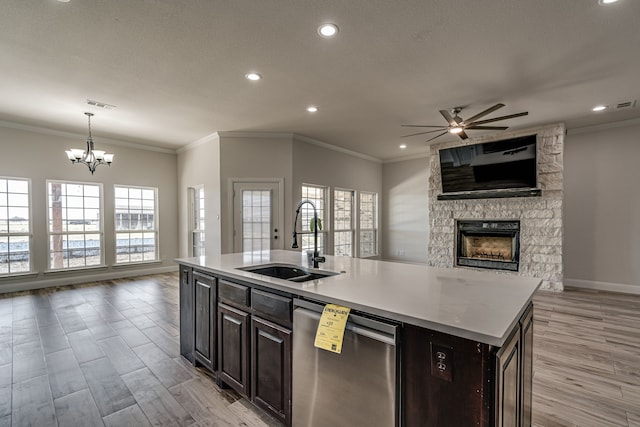 kitchen featuring sink, stainless steel dishwasher, a stone fireplace, a center island with sink, and light hardwood / wood-style flooring