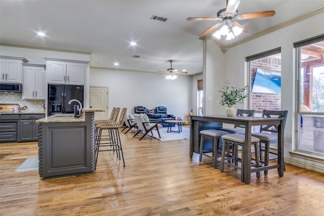 kitchen with gray cabinets, light wood-type flooring, a breakfast bar, a center island with sink, and black fridge with ice dispenser