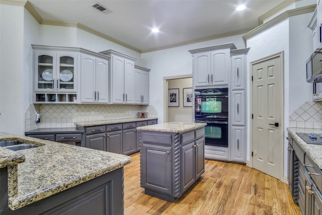 kitchen with ornamental molding, a kitchen island, light hardwood / wood-style flooring, backsplash, and black appliances