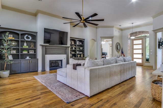 living room featuring crown molding, a tiled fireplace, hardwood / wood-style floors, and ceiling fan