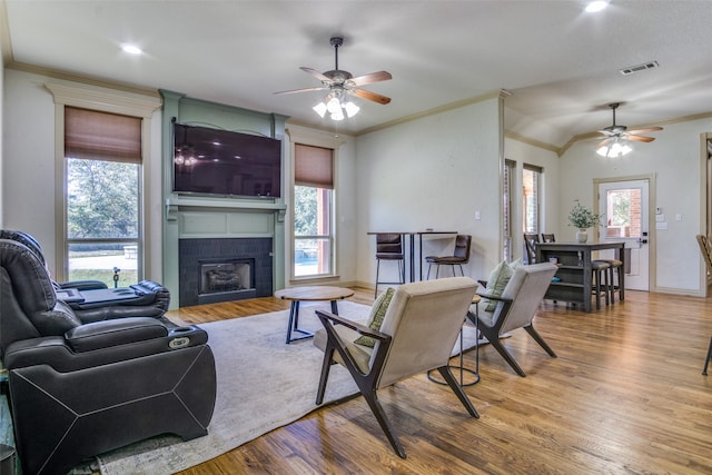 living room with ornamental molding, a tiled fireplace, ceiling fan, and hardwood / wood-style flooring