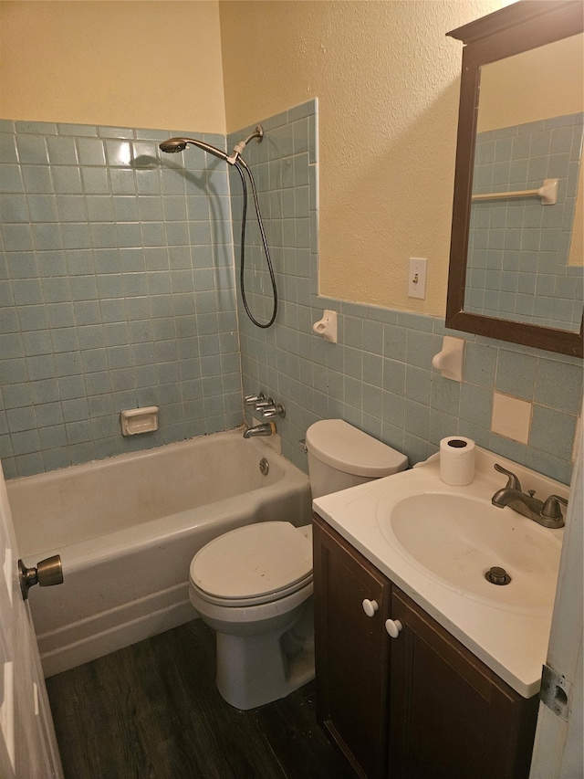 full bathroom featuring tile walls, hardwood / wood-style flooring, tiled shower / bath combo, vanity, and toilet