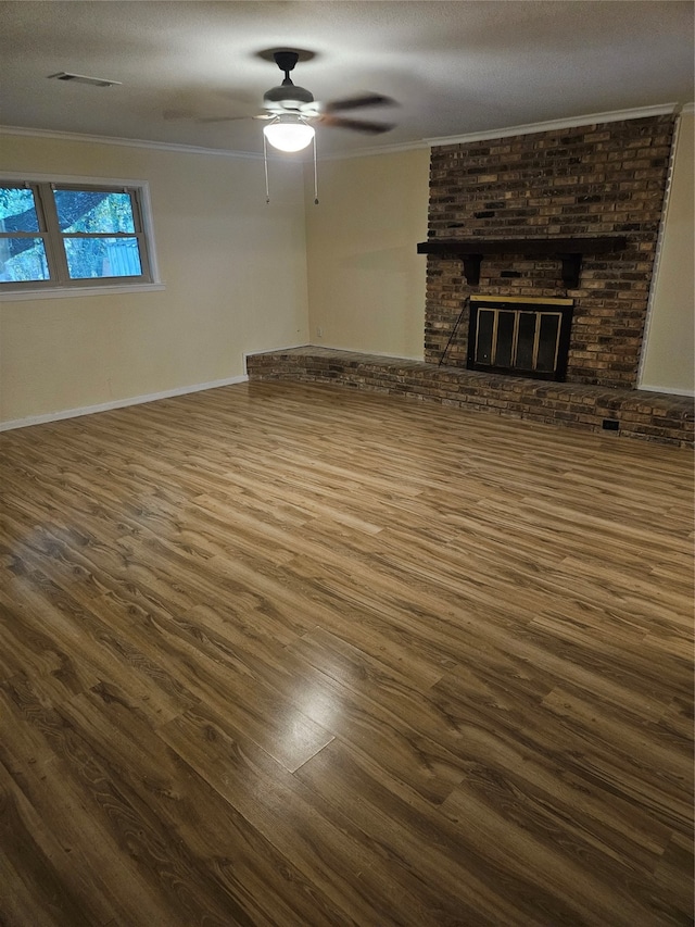 unfurnished living room with dark wood-type flooring, a brick fireplace, a textured ceiling, ceiling fan, and ornamental molding