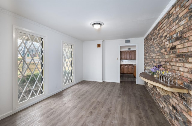 interior space with wood-type flooring, brick wall, and ornamental molding