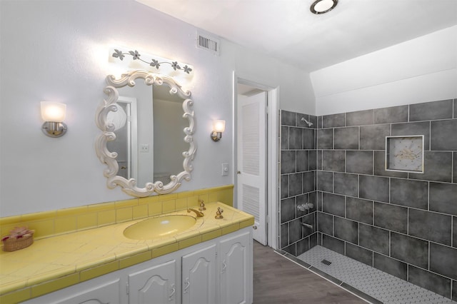 bathroom featuring hardwood / wood-style flooring, tiled shower, and vanity