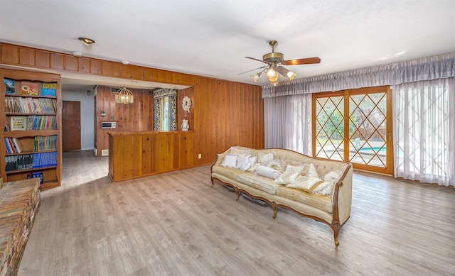 living room featuring ceiling fan, light wood-type flooring, and wood walls