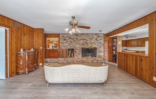 living room featuring ceiling fan, wood walls, a brick fireplace, and light wood-type flooring