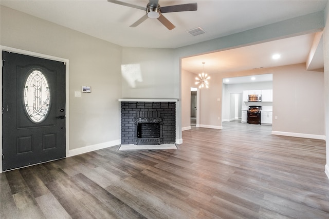 unfurnished living room with ceiling fan with notable chandelier, hardwood / wood-style floors, and a brick fireplace