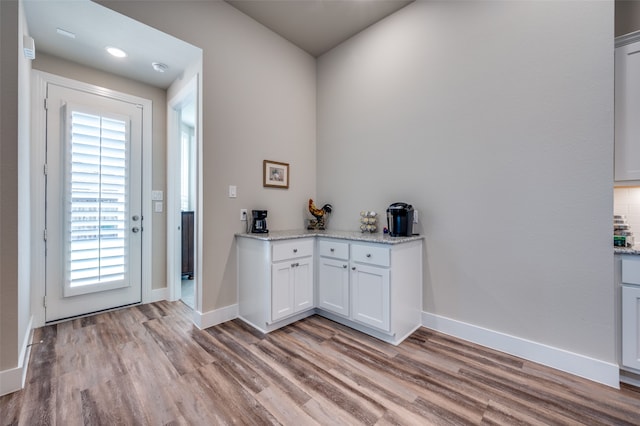 bar featuring white cabinets, decorative backsplash, light hardwood / wood-style floors, and light stone countertops