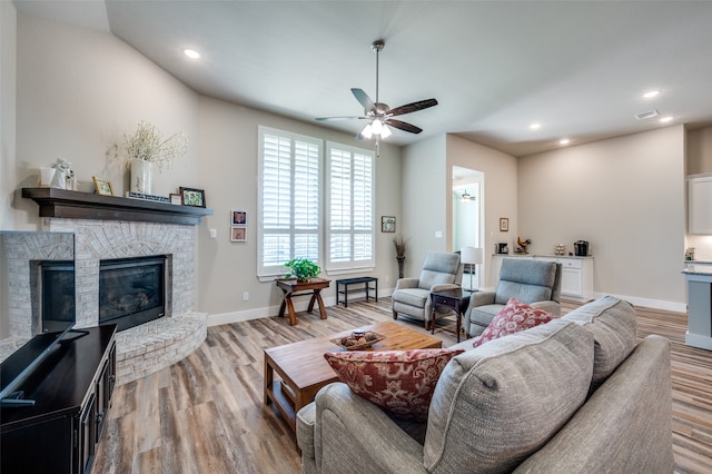 living room featuring ceiling fan, light wood-type flooring, and a fireplace