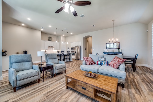 living room featuring ceiling fan with notable chandelier, light hardwood / wood-style floors, and vaulted ceiling