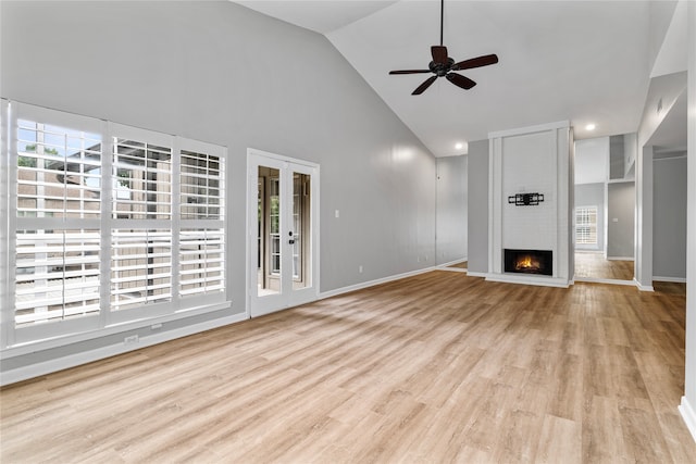 unfurnished living room featuring ceiling fan, french doors, high vaulted ceiling, a fireplace, and light wood-type flooring