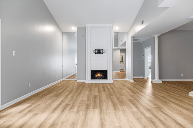 unfurnished living room featuring light hardwood / wood-style floors, vaulted ceiling, a brick fireplace, and ornate columns