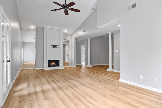 unfurnished living room featuring ceiling fan, ornate columns, high vaulted ceiling, a large fireplace, and light hardwood / wood-style floors