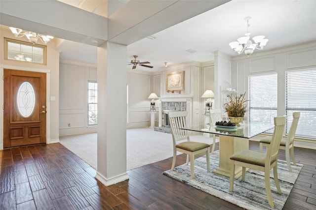 carpeted dining room featuring ornamental molding, a brick fireplace, and ceiling fan with notable chandelier