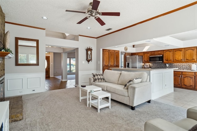 living room featuring a stone fireplace, ornamental molding, a textured ceiling, light hardwood / wood-style floors, and ceiling fan