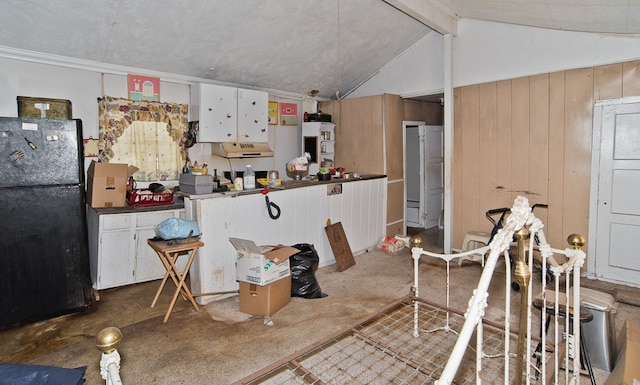 kitchen with vaulted ceiling with beams, white cabinets, wood walls, and black refrigerator