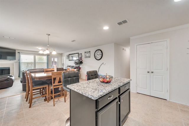 kitchen featuring light stone countertops, pendant lighting, crown molding, a center island, and a notable chandelier