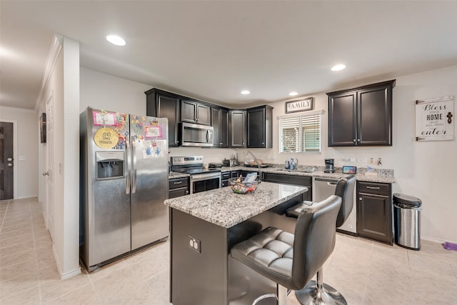 kitchen featuring a breakfast bar, a center island, appliances with stainless steel finishes, ornamental molding, and light stone countertops