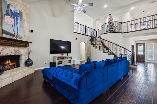 living room featuring ceiling fan, a stone fireplace, a towering ceiling, and dark hardwood / wood-style flooring