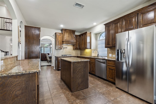 kitchen featuring stainless steel appliances, a kitchen island, light stone counters, and a healthy amount of sunlight