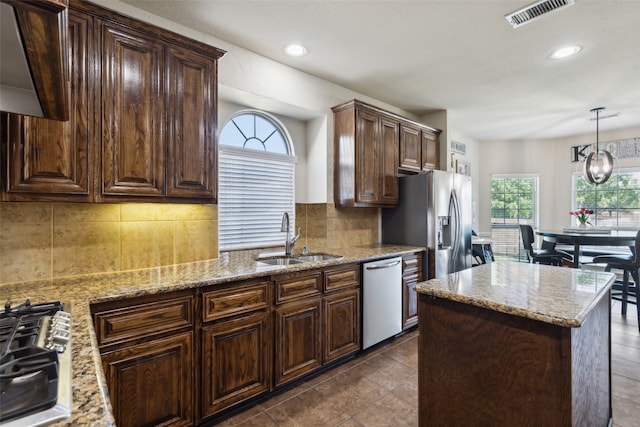 kitchen with light stone countertops, stainless steel appliances, sink, decorative light fixtures, and backsplash