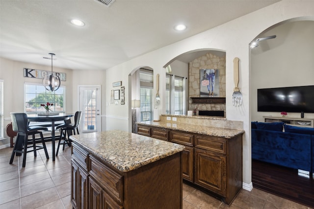 kitchen with an inviting chandelier, a kitchen island, light stone countertops, hanging light fixtures, and light tile patterned floors