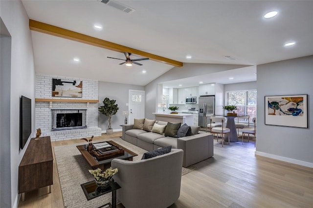 living room with lofted ceiling with beams, light hardwood / wood-style flooring, a brick fireplace, and ceiling fan