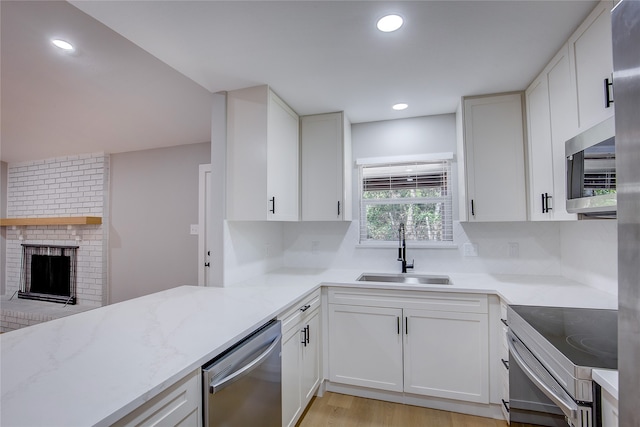 kitchen featuring appliances with stainless steel finishes, a brick fireplace, sink, light hardwood / wood-style floors, and white cabinetry