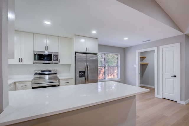 kitchen featuring white cabinetry, stainless steel appliances, light stone counters, lofted ceiling, and light wood-type flooring