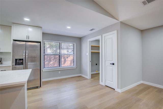 kitchen with light stone countertops, stainless steel fridge, light hardwood / wood-style flooring, white cabinetry, and lofted ceiling