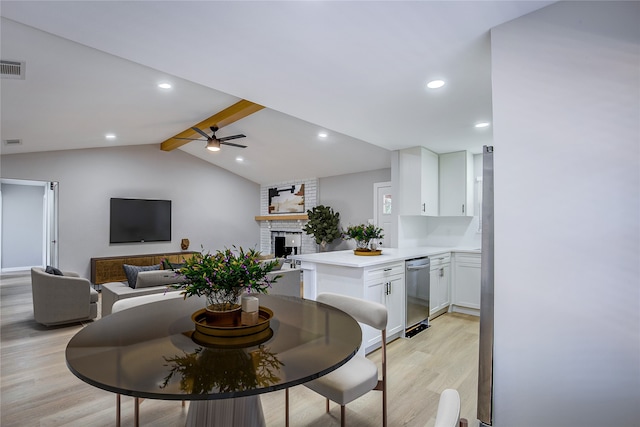 dining space with vaulted ceiling with beams, ceiling fan, a fireplace, and light hardwood / wood-style floors