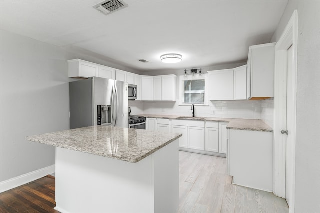 kitchen featuring stainless steel appliances, white cabinetry, a kitchen island, and sink